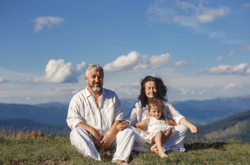 A happy family enjoys a sunny day outdoors, sitting together on a grass field.